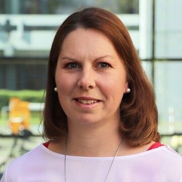 Birgit Czanderle hat kurze braune Haare. Sie trägt ein lilanes Oberteil und blickt in die Kamera.