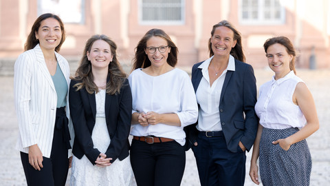 Fünf lächelnde Personen in schicker Kleidung stehen nebeneinander vor dem Schloss der Uni Mannheim.