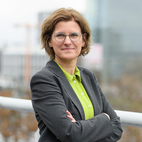Irene Bertschek auf einem Balkon. Sie trägt eine Brille, eine hellgrüne Bluse und einen grauen Blazer.