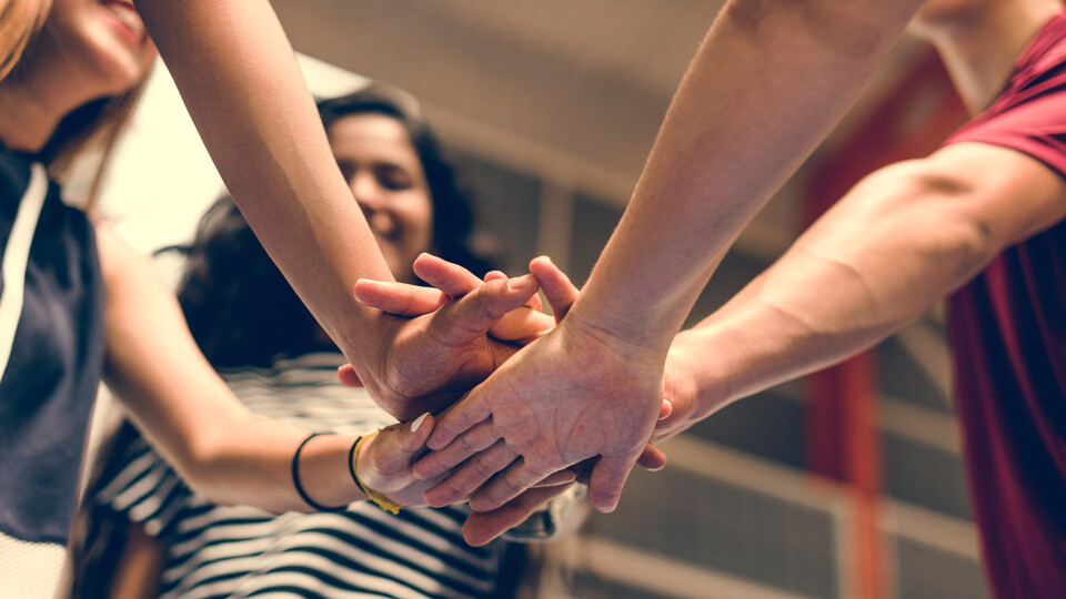 mehrere Menschen strecken ihre Arme in die Mitte und legen ihre Hände aufeinander
