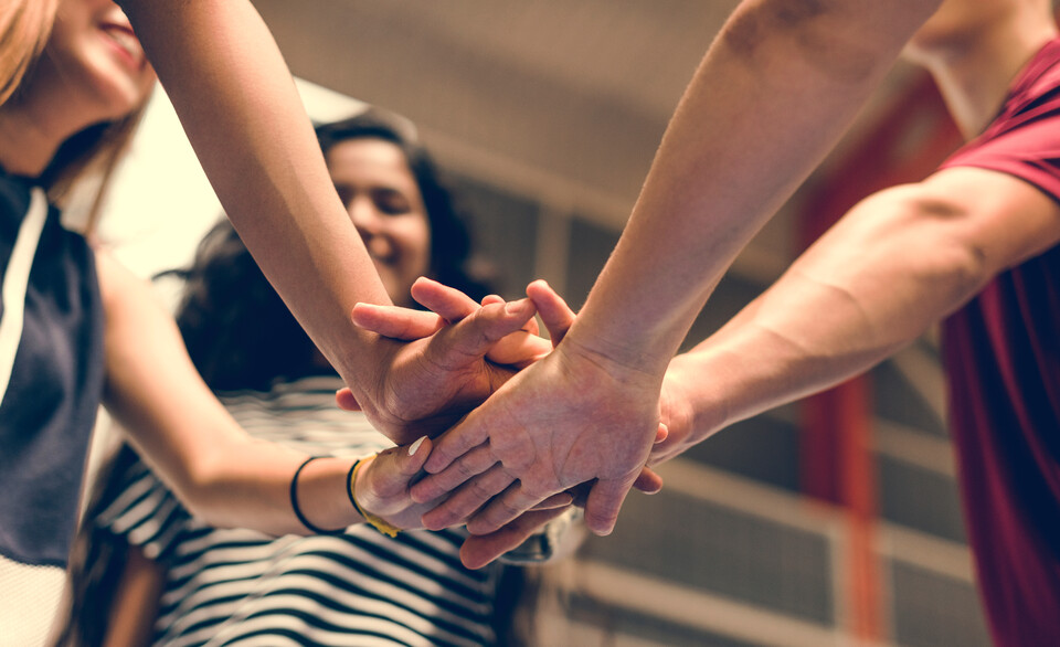 mehrere Menschen strecken ihre Arme in die Mitte und legen ihre Hände aufeinander