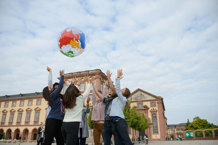 Eine Gruppe von Studierenden wirft eine aufgeblasene Weltkugel in die Luft. Im Hintergrund ist das Schloss.