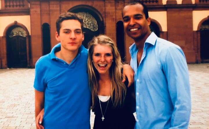 Lea-Sophie Cramer mit langen blonden Haaren und einem schwarzen Shirt steht zwischen zwei Männern in blauen Hemden im Ehrenhof des Schlosses