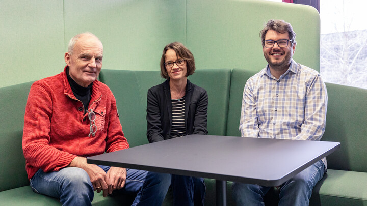 Drei Personen sitzen auf einem grünen Sofa im EduSpace und schauen in die Kamera.