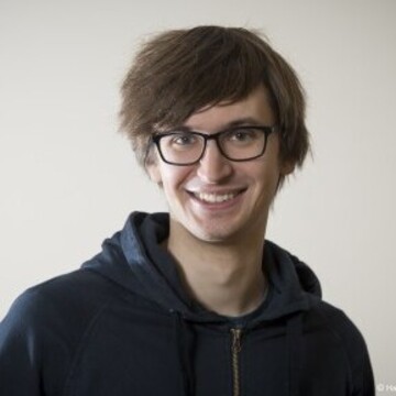Daniel Heck hat kurze braune Haare. Er trägt eine dunkle Brille und ein dunkelblaues Oberteil.