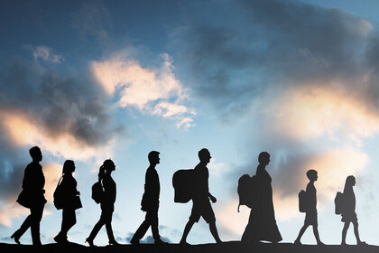 Eine Gruppe von Personen mit Gepäck läuft hintereinander nach rechts. Zu erkennen sind nur ihre wchwarze Silhouetten. Der Himmel ist wolkig.