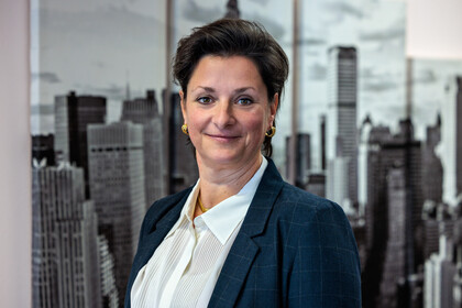 Stefanie Schaefer trägt eine weiße Bluse mit dunkelblauem Blazer und lächelt. 