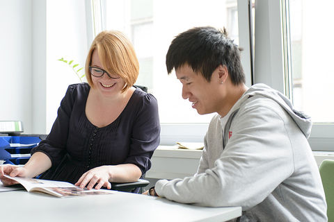 Eine lächelnde Mitarbeiterin der Universität Mannheim zeigt einem jungen Mann eine Broschüre.