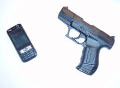 Ein altes Handy mit Bildschirm und Tasten liegt neben einer Pistole.