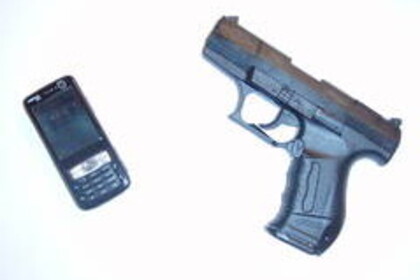 Ein altes Handy mit Bildschirm und Tasten liegt neben einer Pistole.