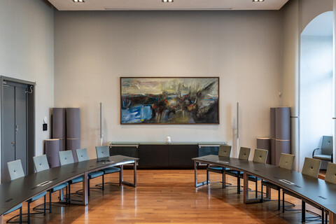 In einem Saal hängt ein großformatiges abstraktes Gemälde in Braun-, Blau und Grautönen und Streifen roter Farbe.
