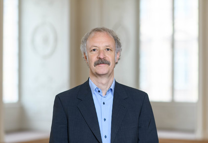 Prof. Dr. Moritz Fleischmann hat graue Haare und einen Schnauzer. Er trägt ein dunkles Jacket und ein gestreiftes Hemd.
