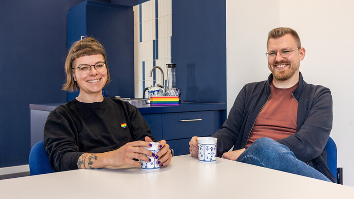 Janina Walker-Emig und Marcel Hörner sitzen an einem Tisch. Sie haben beide Kaffeetassen in den Händen.