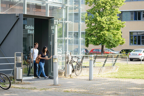 Ein Student und eine Studentin verlassen ein modernes, gläsernes Universitätsgebäude.