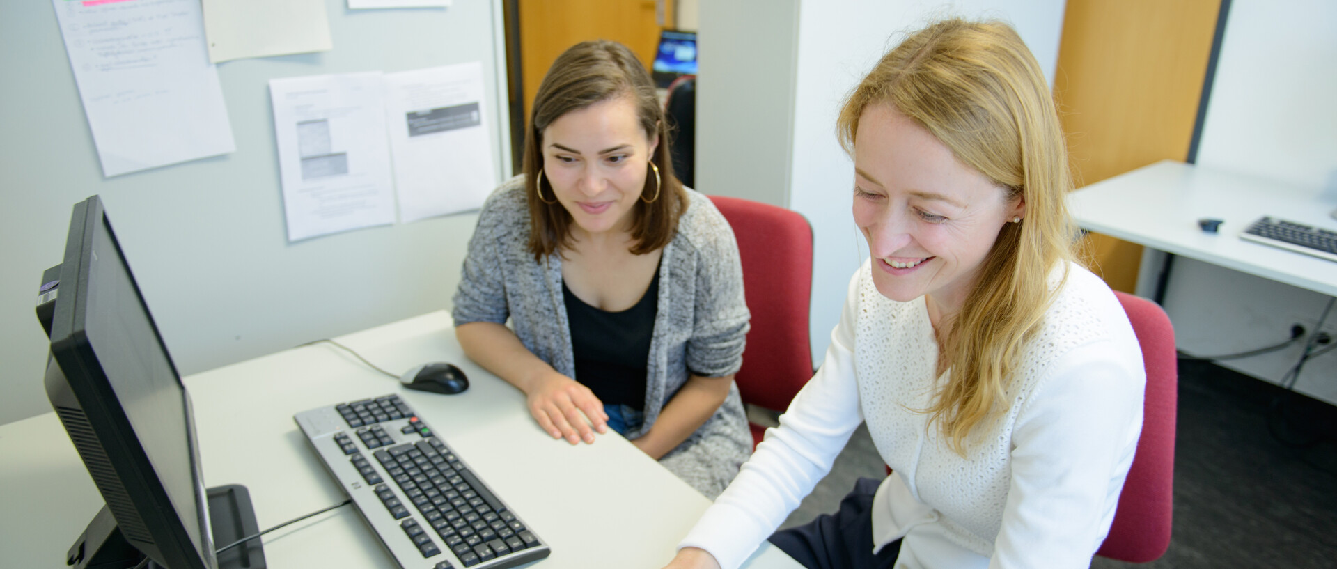 Zwei Personen an Büroarbeitsplätzen mit Computern im Gespräch.