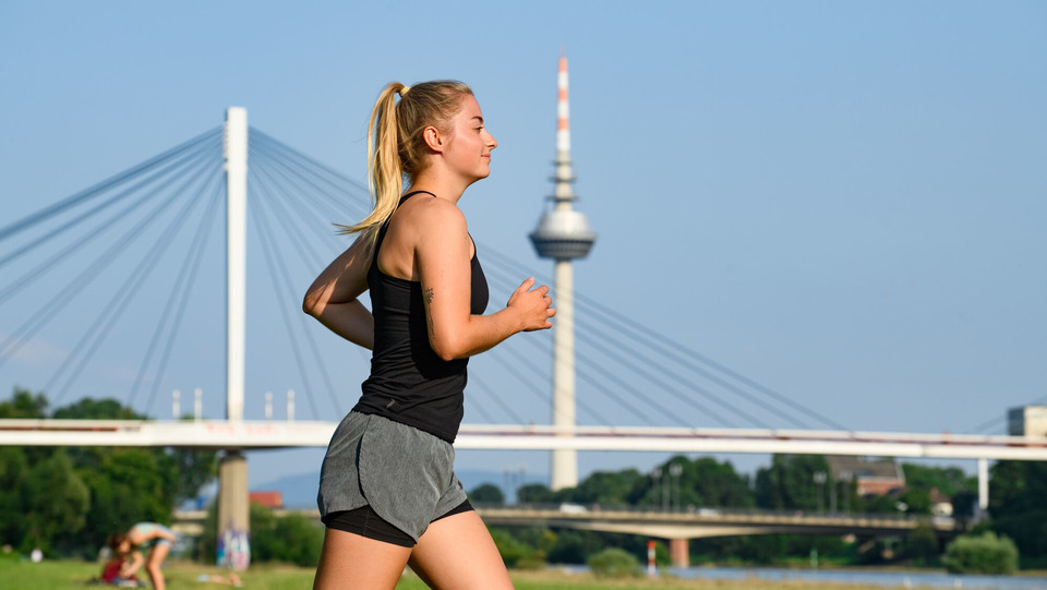 Eine Joggerin am Neckarufer, im Hintergrund der Collini-Steg und der Fernmeldeturm Mannheim