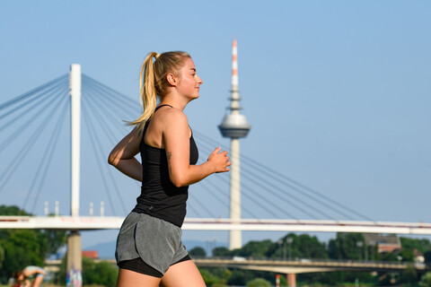 Eine Joggerin am Neckarufer, im Hintergrund der Collini-Steg und der Fernmeldeturm Mannheim