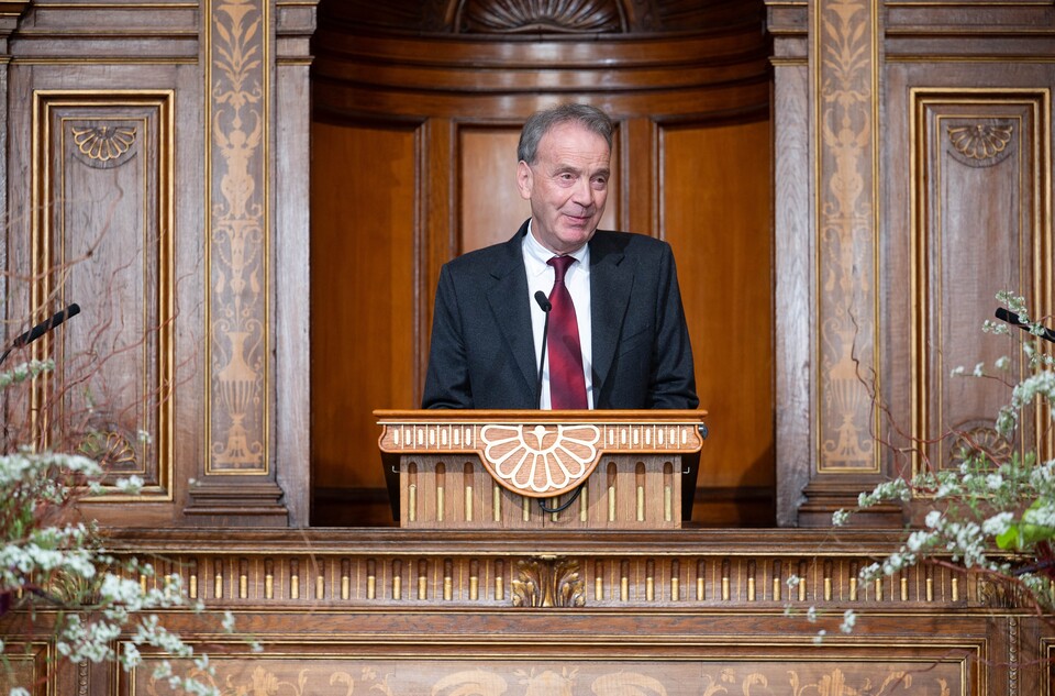 Stefan Reichelstein trägt einen schwarzen Anzug und eine rote Krawatte. Er hält eine Rede.