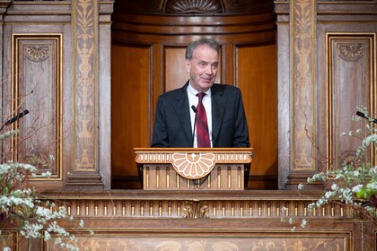 Stefan Reichelstein trägt einen schwarzen Anzug und eine rote Krawatte. Er hält eine Rede.