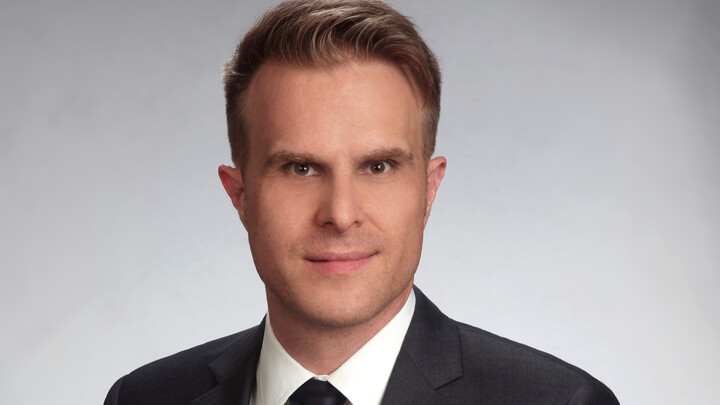Professor Florian Stahl trägt einen schwarzen Anzug und lächelt in die Kamera.