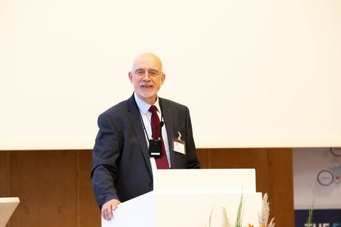 Thomas Puhl trägt einen schwarzen Blazer und steht hinter einem Rednerpult.