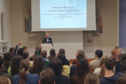 Mehrere Personen hören einem Vortrag von Prof. Dr. Moritz Fleischmann zu, der an einem Pult steht.