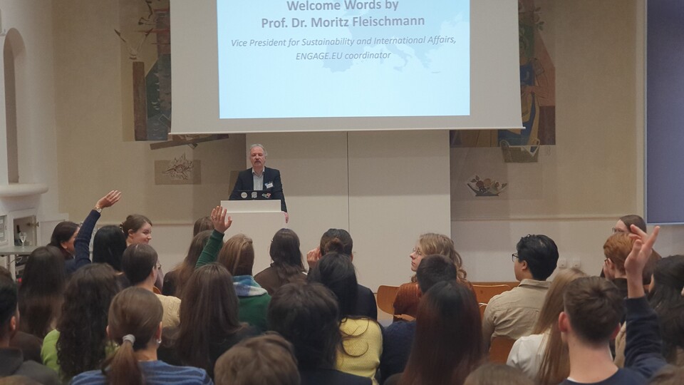 Mehrere Personen hören einem Vortrag von Prof. Dr. Moritz Fleischmann zu, der an einem Pult steht.