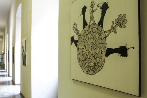 Ein Flur mit Bögen, welche an der rechten Wand entlanglaufen, ist geschmückt mit Kunstwerken, bestehend aus Zeitungscollagen und Farbklecks-Figuren.