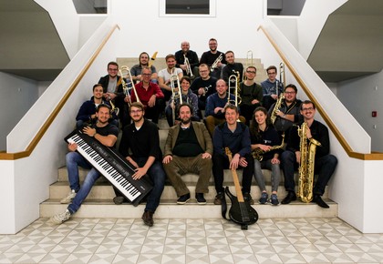 Mitglieder eines Orchesters sitzen mit ihren Instrumenten auf einer Treppe.