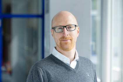 Portrait von Florian Keusch. Er trägt einen grauen Pullover über einem weißen Hemd.