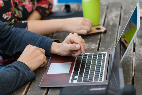 Zwei Studierende sitzen an einem Holztisch vor einem Laptop.
