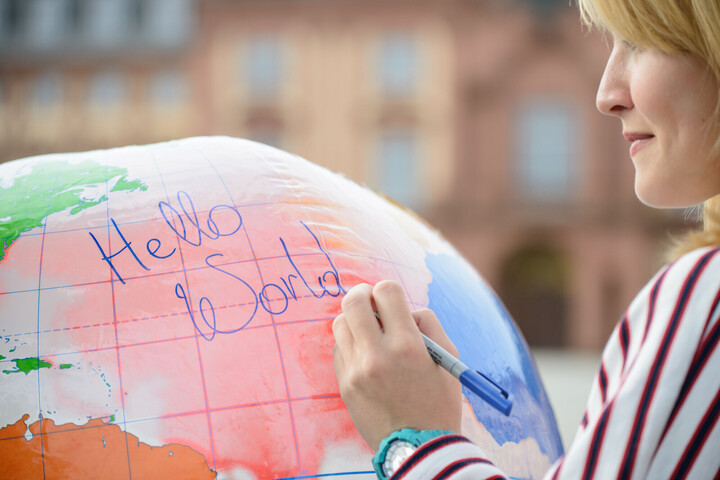 Eine Frau schreibt "Hello World" auf eine große aufgeblasene Weltkugel.