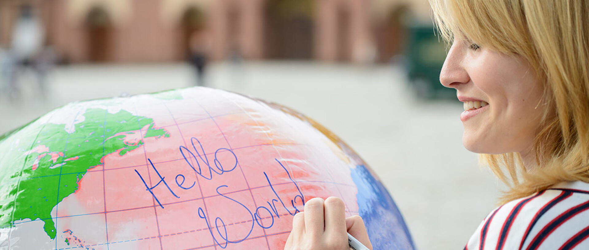 Eine junge Frau schreibt auf eine Weltkugel die Wörter "Hello World".