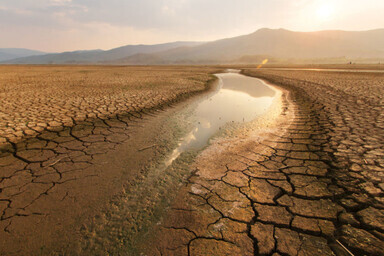 Ausgetrockneter See mit Wasserresten, drum herum Wüste. Die Sonne scheint.