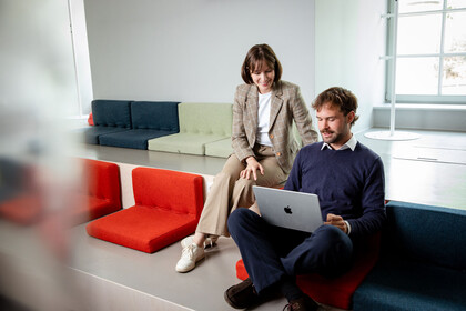 Zwei Forschende sitzen im exLAB zusammen und betrachten etwas auf dem Laptop. Die Frau trägt einen modichen Hosenanzug. Der Mann dunkle Hosen und einen dunklen Pulli.