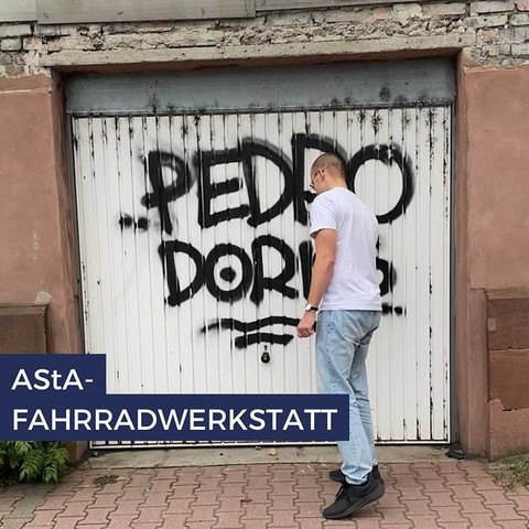Student steht vor einer alten Garage. Die Garagenwand ist mit Graffiti besprüht. Link: Instagram Fahrradwerkstatt AStA
