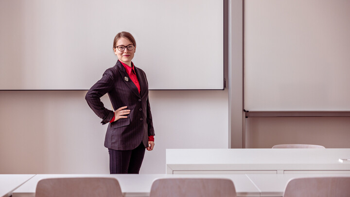 Anna-Maria Rohe steht in einem Seminarraum der Universität neben einem Tisch.
