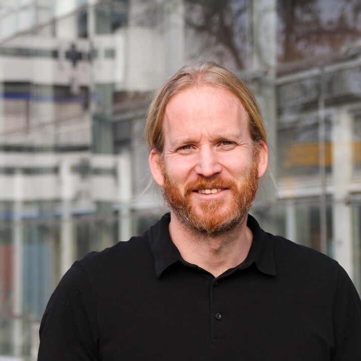 Portrait eines Mannes mit schwarzem Hemd, der vor dem B6-Gebäude steht.