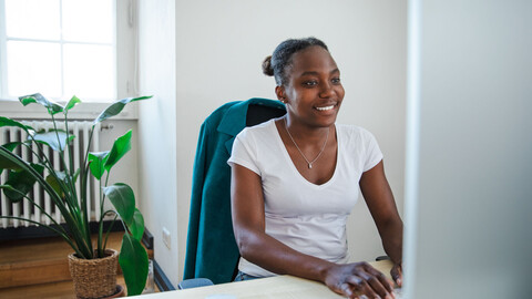 Eine Mitarbeiterin sitzt lachend vor einem Bildschirm im Büro.