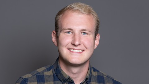 Tobias Kreuz. He is wearing a blue-green checkered shirt and is standing in front of dark grey wall.