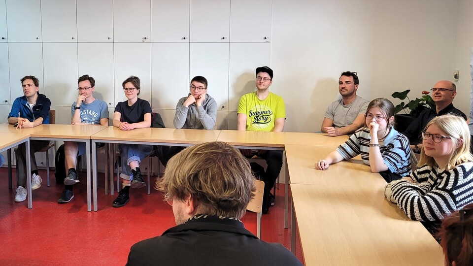 Die Teilnehmenden der Summer School sitzen an einem U-förmigen Tisch und hören aufmerksam zu.