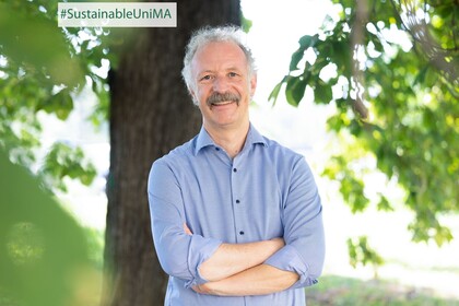 Prof. Dr. Moritz Fleischmann. Er lächelt, sein Hemd ist hellblau gestreift und er hat einen Schnurrbart.