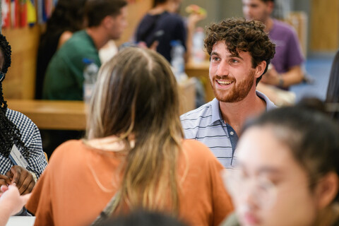 Studierende sitzen an einem Tisch in der Mensa und unterhalten sich.