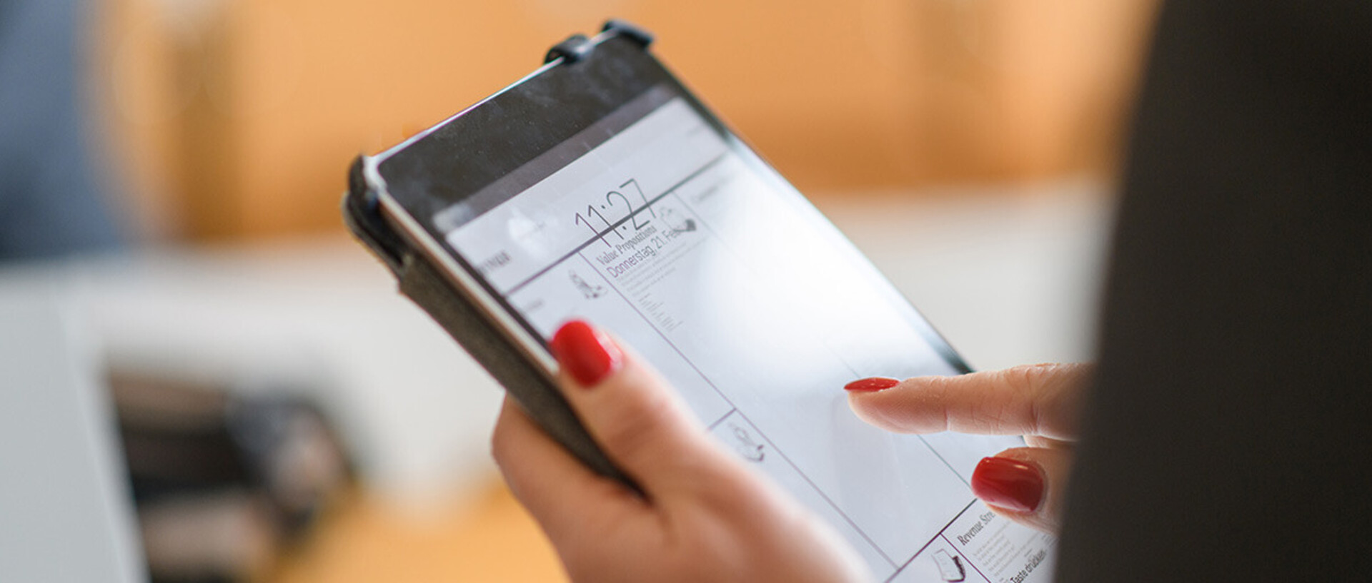 Eine Person mit lackierten Nägeln hält ein Tablet in der Hand.