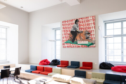 Exlab-Raum der Universität Mannheim. Viele bunte Sitzgelegenheiten und ein großes Gemälde an der Wand von einer Person, die auf einem Tiger sitzt.