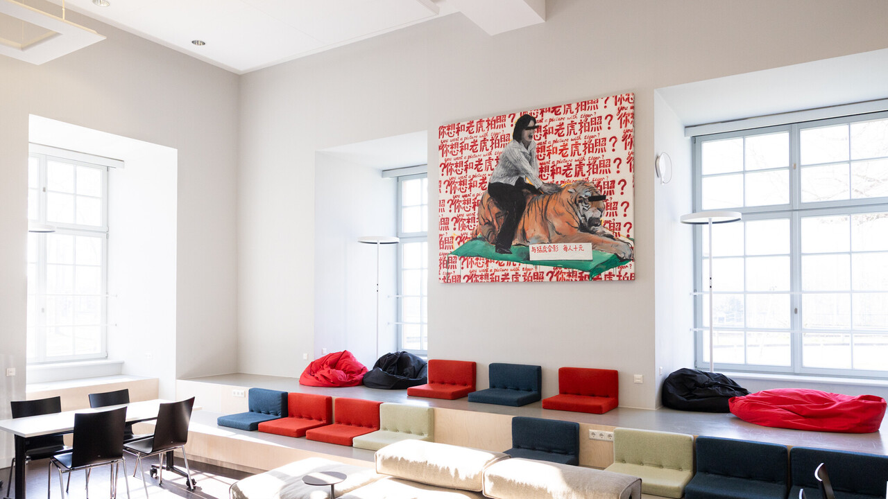 Exlab-Raum der Universität Mannheim. Viele bunte Sitzgelegenheiten und ein großes Gemälde an der Wand von einer Person, die auf einem Tiger sitzt.