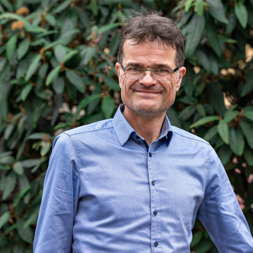 Bernward Gesang. Bernward Gesang trägt ein blaues Hemd und steht vor einem grünen Hintergrund.