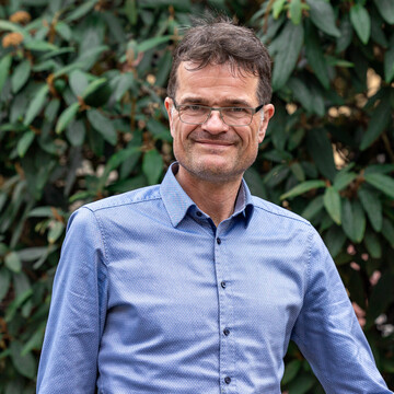 Bernward Gesang. Bernward Gesang trägt ein blaues Hemd und steht vor einem grünen Hintergrund.