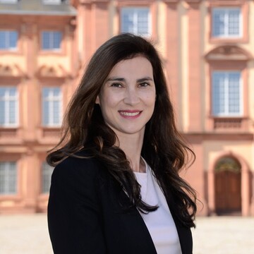 Christina Vonhoff hat lange braune Haare. Sie trägt ein weißes Oberteil und einen schwarzen Blazer.