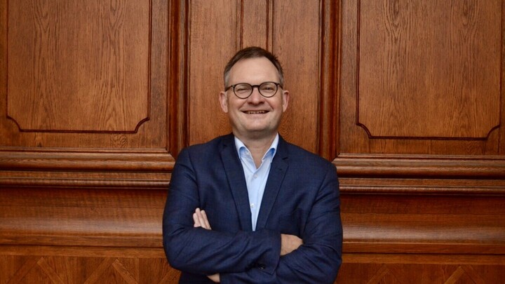 Porträtfoto von Prof. Dr. Philipp Gassert. Er steht vor einer braunen Holztür, lächelt und verschränkt die Arme.